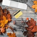 Workspace with laptop, maple yellow and red leaves, credit card on grey wooden background. Flat lay, top view.