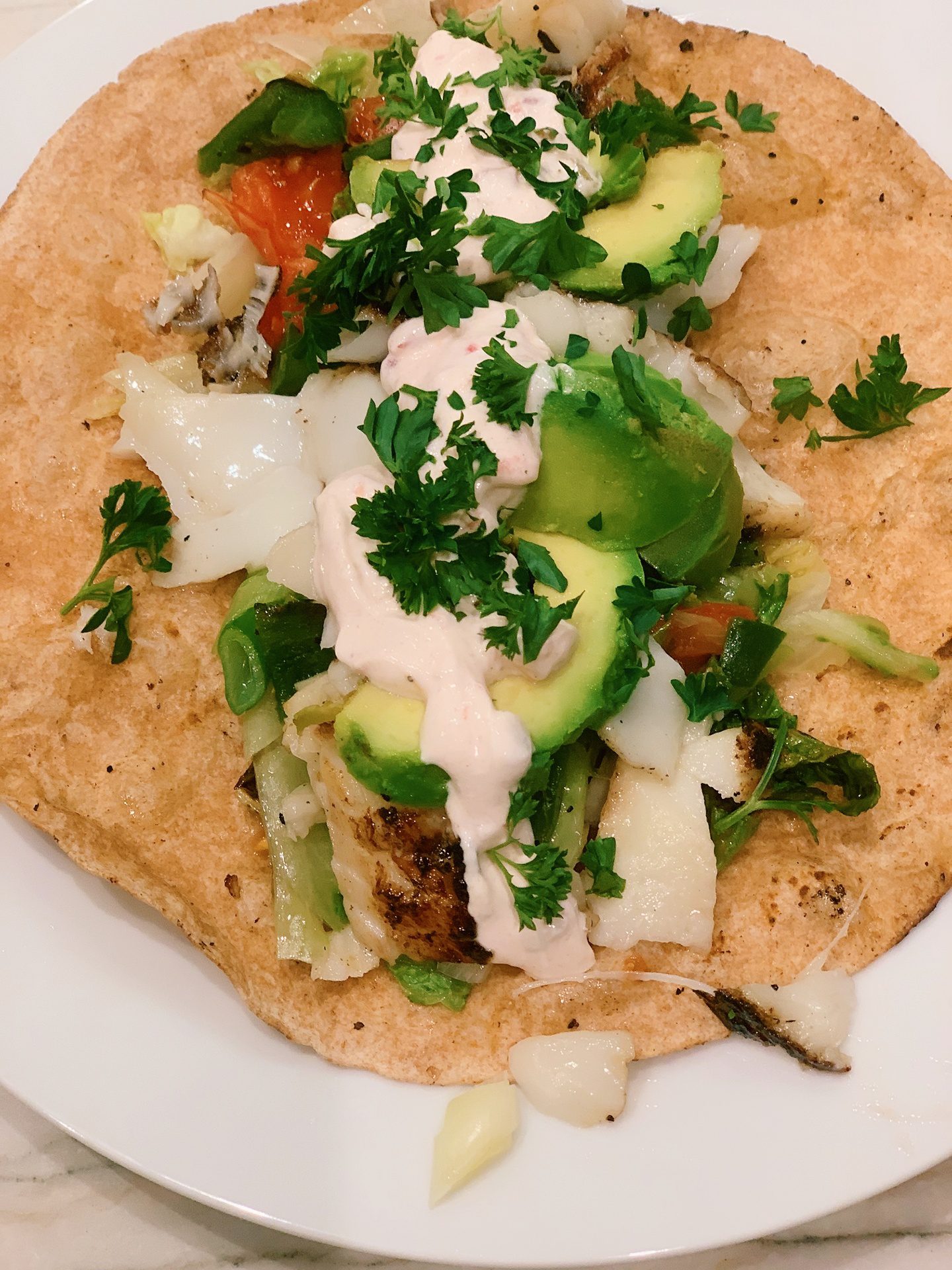 Fish in a soft tortilla with cilantro, crema, tomato, lettuce