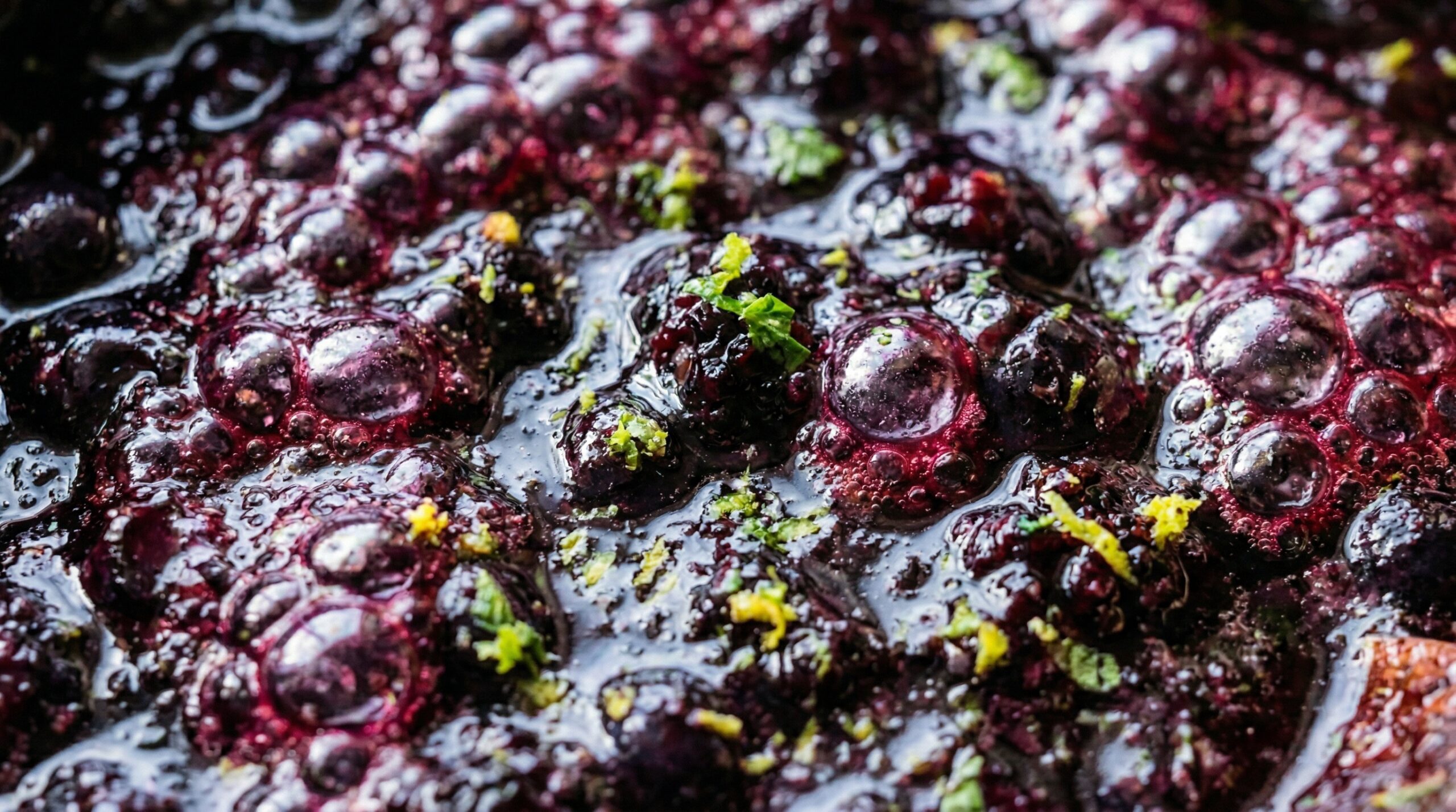 Macro detail of a thick, bubbling mixture of fresh blueberries, blackberries, and granulated sugar actively simmering in a small copper saucepan
