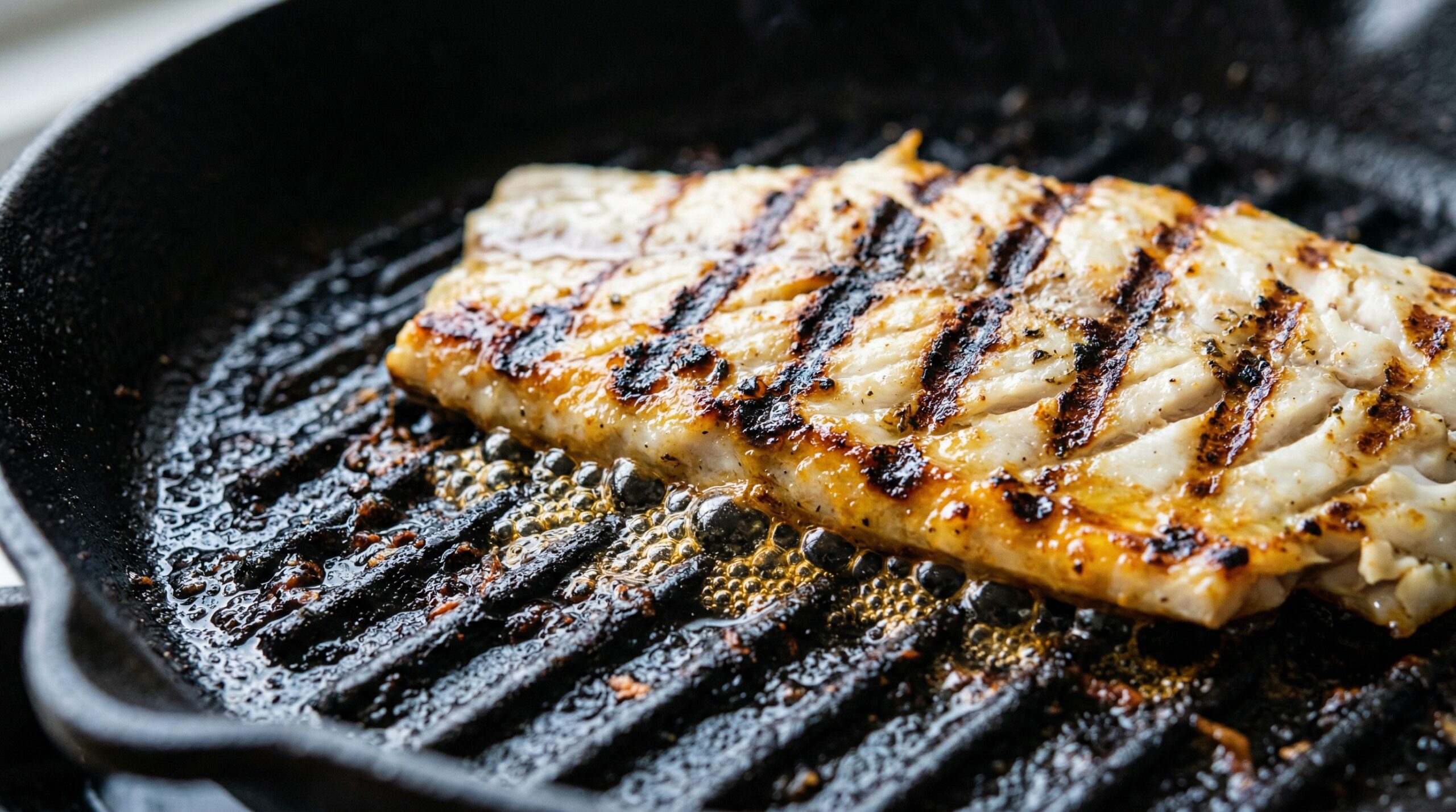 Macro detail of sea bass searing on a cast-iron grill pan with architectural marks